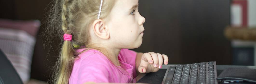 A teacher guiding children at a computer, demonstrating safe, supervised online learning in a classroom environment